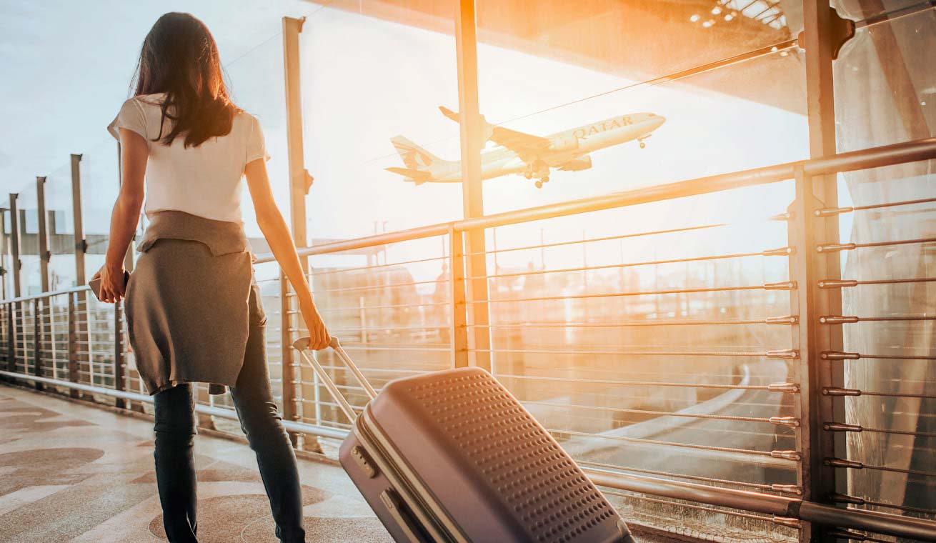  Image of the rear view of a business traveler with a luggage while waiting for her flight at the airport.