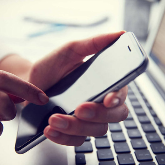 Image of a man using a mobile phone with a laptop seen in the background